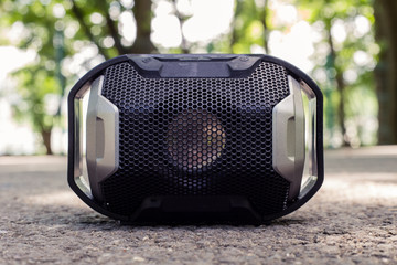 Small plastic portable speaker with black detailed grill placed on ground with blurred background – Wireless device for playing music outdoor