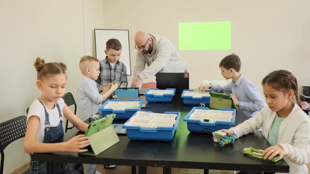 Group of young kids try to design their first plastic robots and cars at the engeniiring lesson slow motion