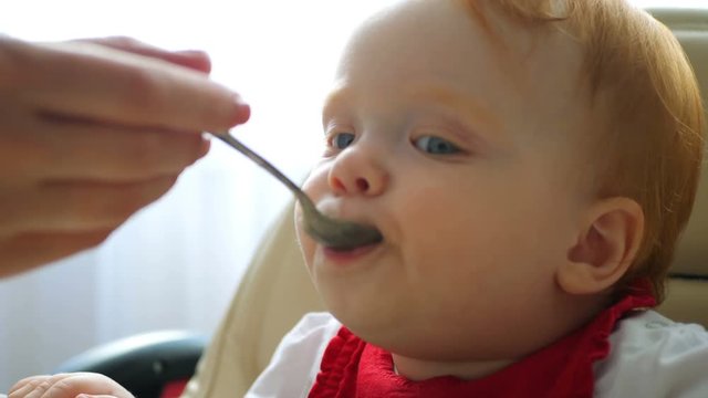Baby eating puree with spoon. Close up of infant baby face eat baby food. Mother feeding child with porridge. Little girl eating porridge