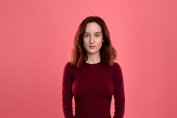Obraz premium Portrait of a beautiful brunette girl standing on a dark pink background. Model confidently looks at the camera.