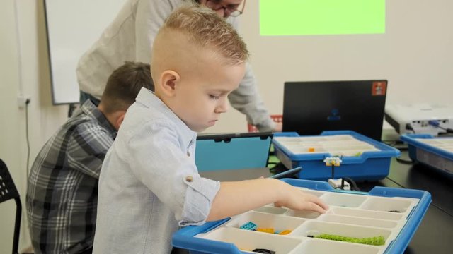 Curious blond caucasian kid experiences how to construct the plastic robot toy at the class slow motion