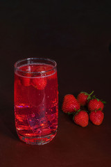 Drink with ice from strawberries on a dark background. Fresh strawberry cocktail. Fresh summer cocktail with strawberry and ice cubes. Glass of strawberry soda drink on dark background.