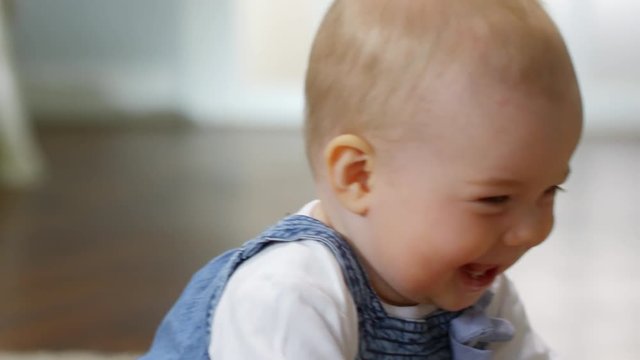 Tilting close-up shot of adorable Caucasian baby girl sitting and playing with wooden zebra toy, laughing with delight and nibbling on it