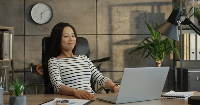 Young Asian female office worker working on the laptop computer, tapping and resting in the comfortable chair. Indoor.