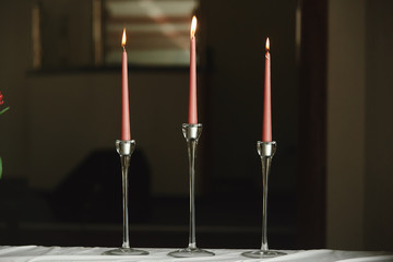 Burning candles on bronze candlestick against dark background at home.candles in the interior. Vintage style. Calm romantic atmosphere. Horizontal image for design.