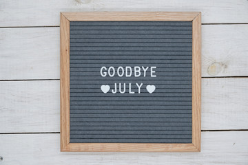 text in English goodbye July and a heart sign on a gray felt Board in a wooden frame