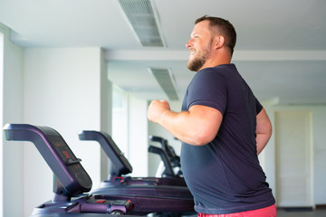 chubby man walking on running track, warming up on gym treadmill.