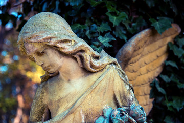 A fragment of ancient sculpture angel in a golden glow in the old cemetery. Symbol of love, invisible forces, purity, enlightenment, ministry. Chariot. Vintage retro style.