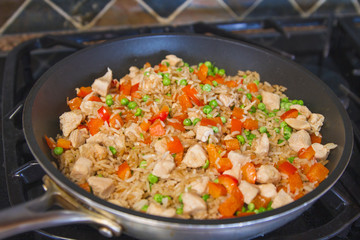 Garlic chicken fried rice with peppers and peas in a frying pan on a stove; homemade chicken fried rice cooking on the stove