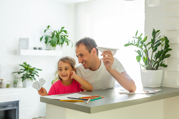 Handsome father and his cute little daughter are playing with paper planes and smiling while spending time together