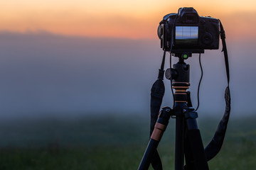 black digital camera on tripod shooting foggy morning landscape at summer with selective focus