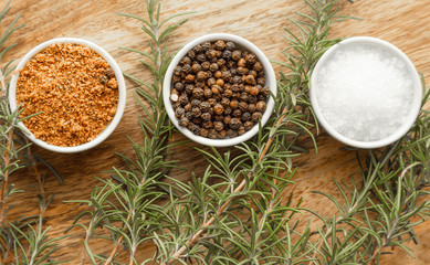 Close-up photo of colored spices, salt, pepper and rosemary in bowls on wooden board