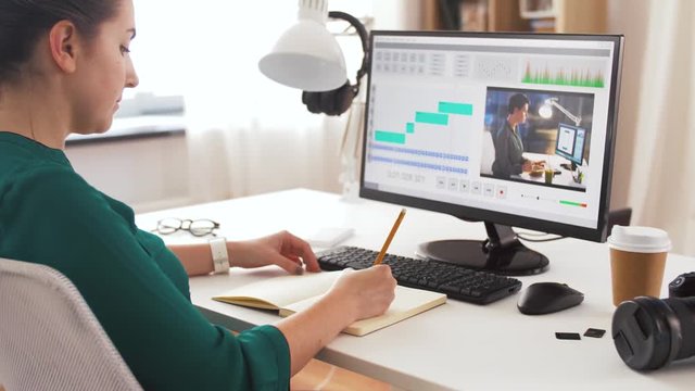 technology, post production and vlog concept - woman working in video editor program on laptop computer writing to notebook at home office