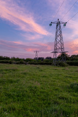 A portrait view of power lines and pylons leading off into the distance with an incrediable sunset overhead.