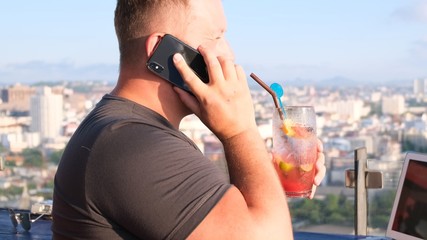 man talking on the phone and working on a computer in a cafe with a beautiful view