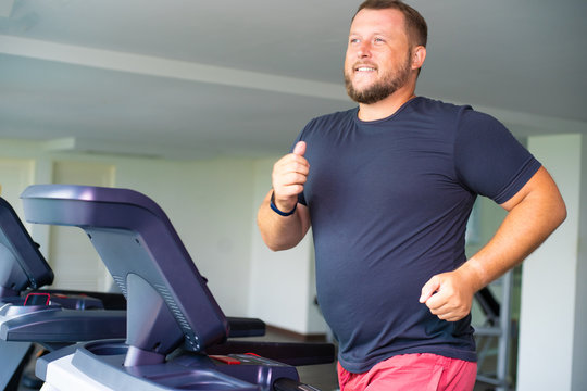 smiling full male runs on a treadmill in a gym. concept of weight loss and sport. side view.