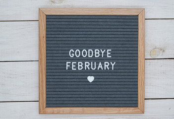 text in English goodbye February and a heart sign on a gray felt Board in a wooden frame