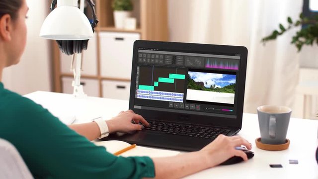technology, post production and vlog concept - woman working on travel video in editor program on laptop computer and writing to notebook at home office