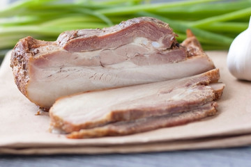 Baked slice of pork peritoneum with layers of fat with vegetables on a wooden table.