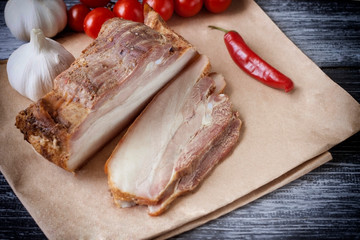 Baked slice of pork peritoneum with layers of fat with vegetables on a wooden table.