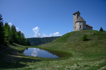 idyllic church St. Vigilius on hill with alpine lake sky and trees in italia