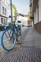 Fototapeta na wymiar Classic bicycle with blue wheels on city street. Urban transport concept. Parking bike in town. Antique bike on street. Travel and tourism concept. Urban style.