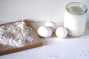 Flour, milk and eggs on a wooden white table.