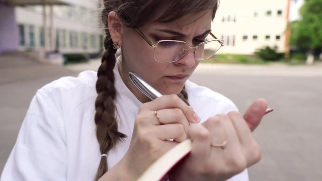 Portrait of a cute young woman in glasses and with long fair hair.carefully writes something in a notebook.She is a strict teacher or a smart student or a qualified doctor, schoolgirl, graduate studen