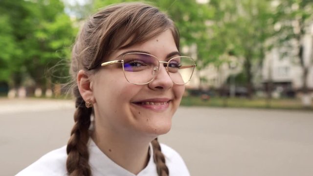 Portrait of a cute young smiling woman in glasses and with long fair hair looking straight in the camera. She is a strict teacher or a smart student or a qualified doctor, schoolgirl, graduate student