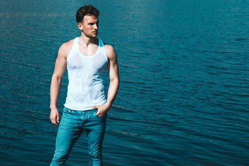 Handsome topless male model in jeans walking on the beach. Outdoor shot.