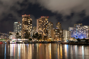 Fototapeta na wymiar Honolulu night cityscape with lights reflected in water on a cloudy night