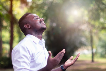 African man praying for thank god with light flare in the green nature - obrazy, fototapety, plakaty