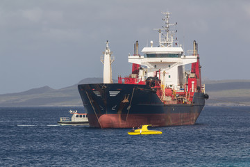 Cargo ship getting in anchoring position by a tugboat for making a delivery of industry parts in...