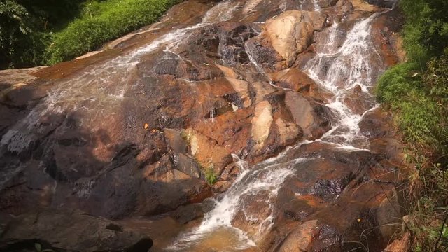 Small beautiful cascade waterfall in the picturesque jungle rainforest. Stream of mountain fresh water flows and falls on the mossy stones on a hot sunny day. Thailand, Koh Samui, Namuang waterfall.