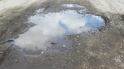 Puddle with reflection of clouds on a dirt road