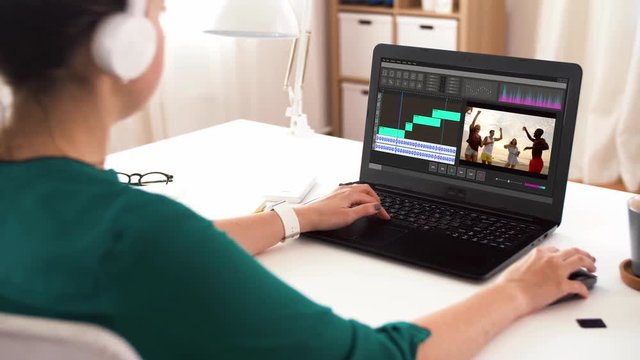 technology, post production and vlog concept - woman in headphones working on video of summer vacation in editor program on laptop computer at home office