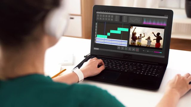 technology, post production and vlog concept - woman in headphones working on video of summer vacation in editor program on laptop computer at home office