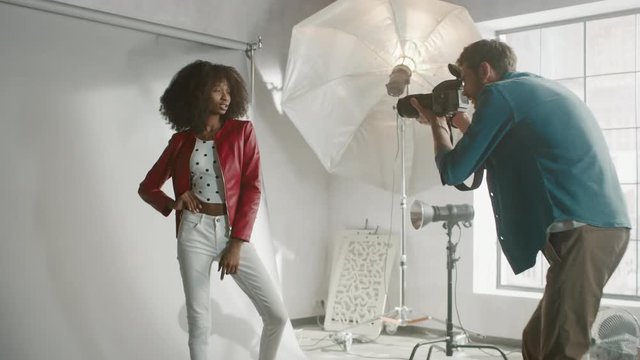 Backstage of the Photo Shoot: Make-up Artist Applies lipstick Makeup on Beautiful Black Model with Lush Curly Hair. Girl Fools Around and Makes Funny Faces. Fashion Magazine Studio Photoshoot