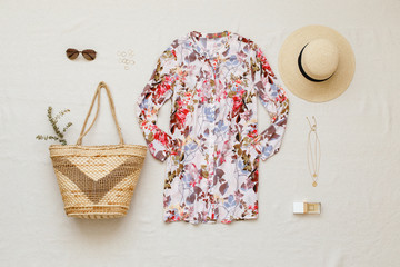 Floral shirt dress, straw boater hat, wicker beach bag, sunglasses, gold necklace and perfume on...