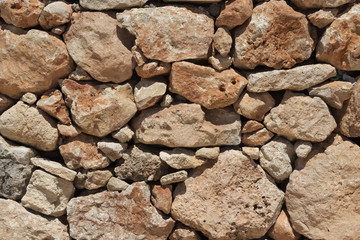 Natural beige stone wall (masonry) created by stacking stones on top of each other with varying stone sizes.