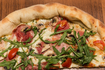top view closeup half of pizza with arugula, ham, and tomatoes