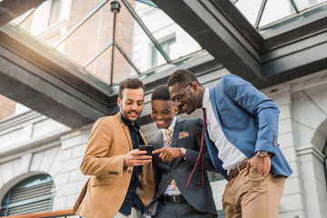 three young friendly men in suits are looking into the smartphone
