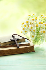 wooden cross, old religion books and chamomile flowers on wooden table, abstract nature background....