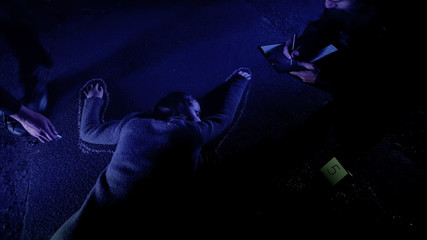Policeman fixing position of corpse with chalk, crime scene investigation