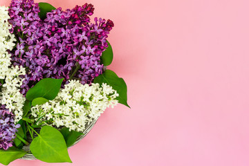 Basket with branches of white and purple lilac on a pink background with empty place for text.