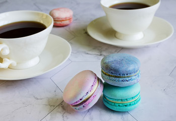 multicolored macarons on a marble table. white cups of tea or coffee. breakfast with dessert