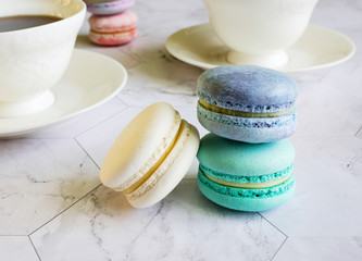 multicolored macarons on a marble table. white cups of tea or coffee. breakfast with dessert