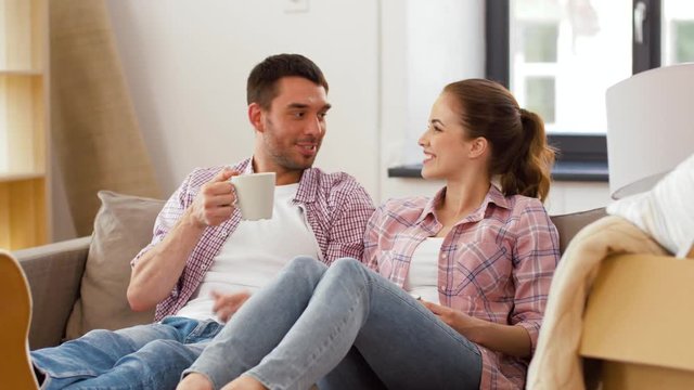 moving, people, repair and real estate concept - happy couple sitting on sofa and drinking coffee at new home