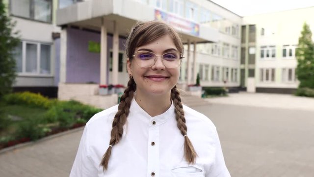 Portrait of a cute young smiling woman in glasses and with long fair hair looking straight in the camera. She is a strict teacher or a smart student or a qualified doctor, schoolgirl, graduate student