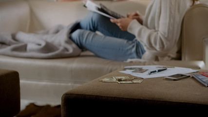Money on table, woman lying on couch and counting expenses, planning budget